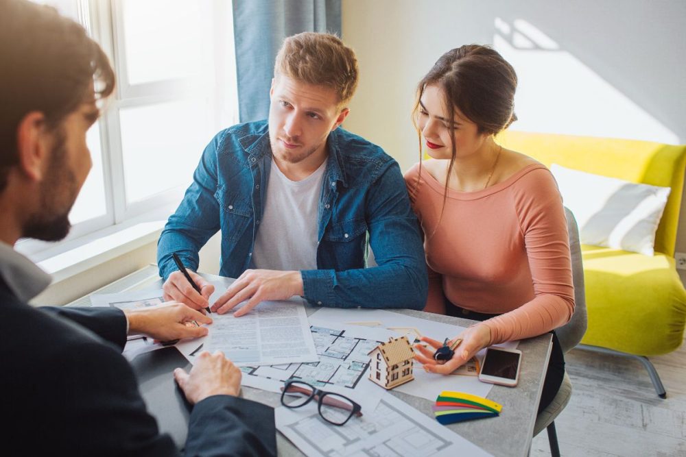 Young couple discussing home plans with a property advisor, exploring is it cheaper to build or buy a house.