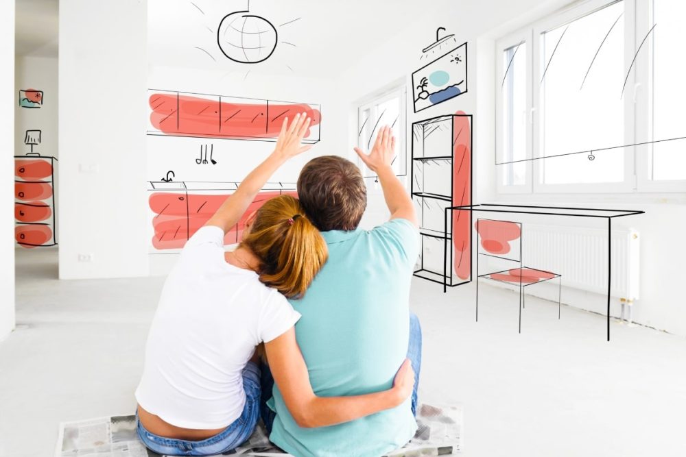 A couple sitting in an empty room visualising their future home's interior, as depicted by drawn illustrations of furniture and decor on the walls around them.
