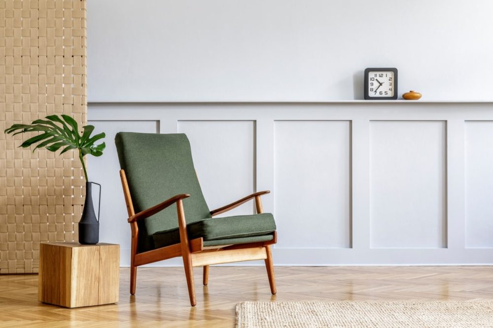 A minimalist home staging setup for sale, featuring a decluttered room with a stylish green mid-century modern armchair as the focal point. Beside it, a chic vase with a monstera leaf and a small wooden side table complement the clean and spacious feel, perfectly embodying decluttering and home staging for sale.