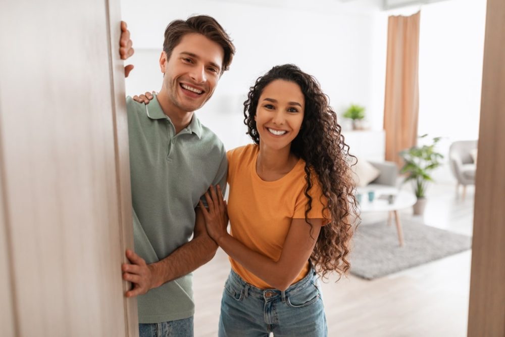 A smiling couple welcoming a visitor at the front door. This is a visual representation of tenants and property managers doing regular inspections.