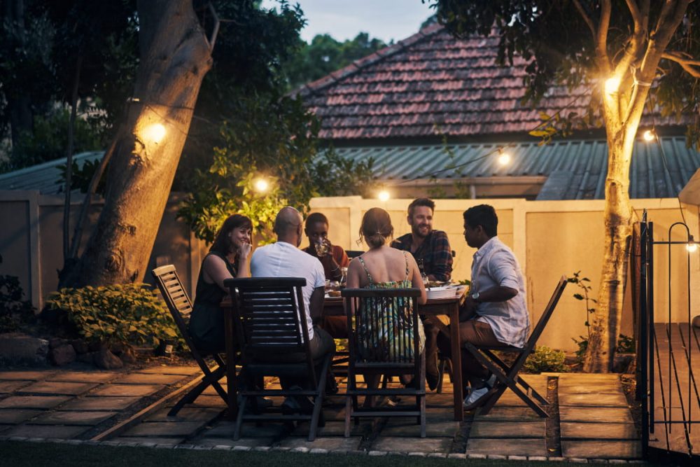 A group of friends enjoying a relaxed outdoor dinner in Ellenbrook, surrounded by warm lighting and greenery, showcasing the suburb’s vibrant community atmosphere.