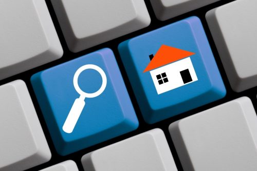 Keyboard with magnifying glass and house symbols, illustrating the concept of becoming a real estate agent.