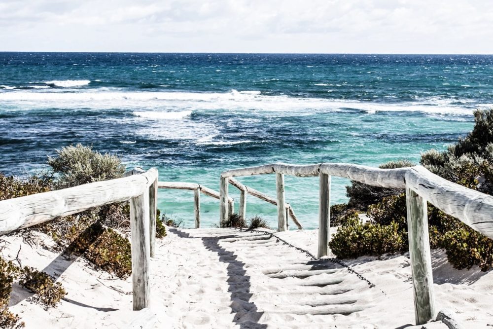 Moving to Australia Checklist: How to Prepare for a Stress-Free Move 1 Wooden steps leading down to a bright turquoise beach in Australia, symbolising a fresh start for new arrivals.