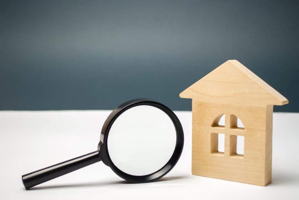 A close-up of a wooden house and magnifying glass, implying the detailed examination that occurs during property viewings and inspections.