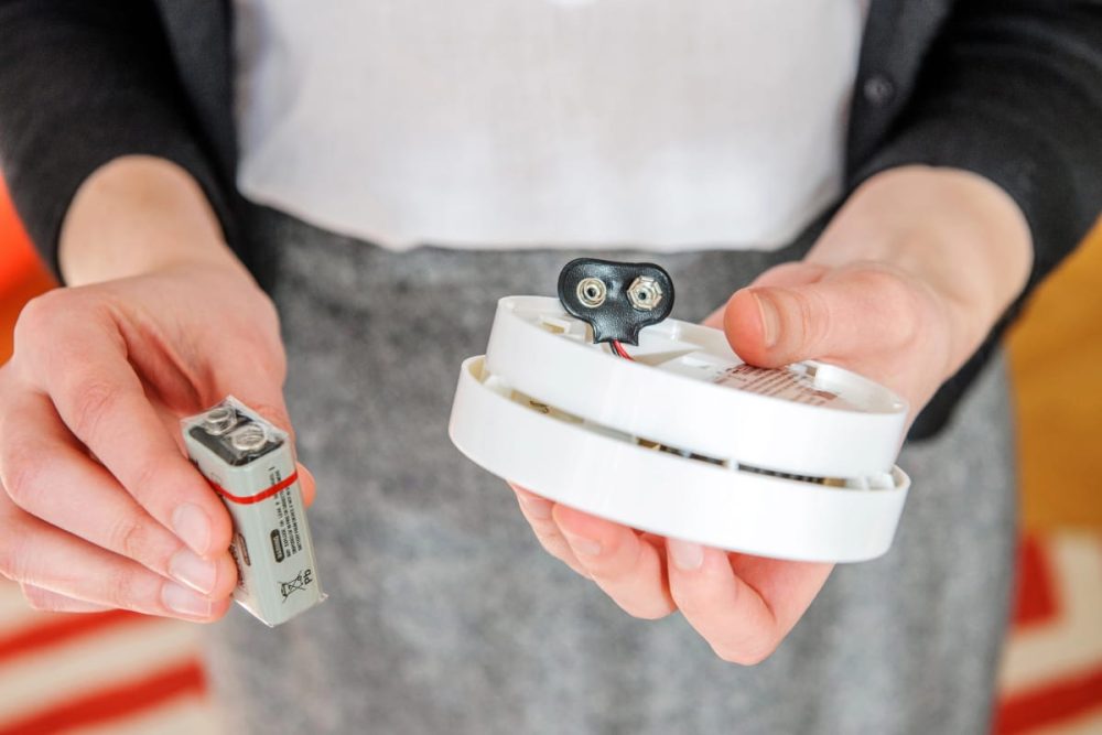 Tenant replacing a smoke alarm battery as part of rental property maintenance.