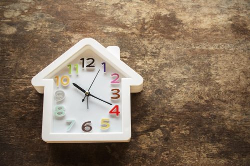 A house-shaped clock on a wooden surface, symbolising the time it takes to sell a property in Australia. Learn more about how long does it take to sell a house in the current market.