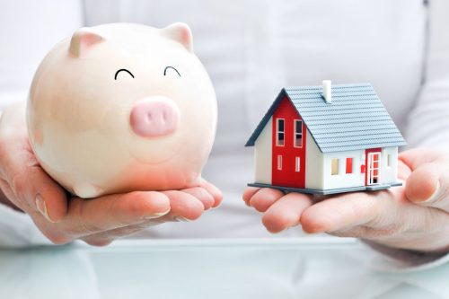 Piggy bank and house model in open hands, capturing the essence of real estate strategy: Timing the Market Vs Time in the Market.