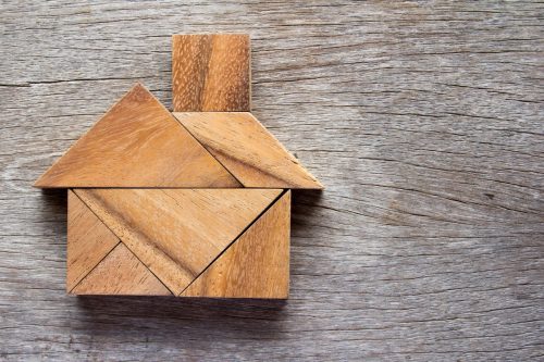 Wooden tangram puzzle in the shape of a house, conveying the idea of how to put an offer on a house.